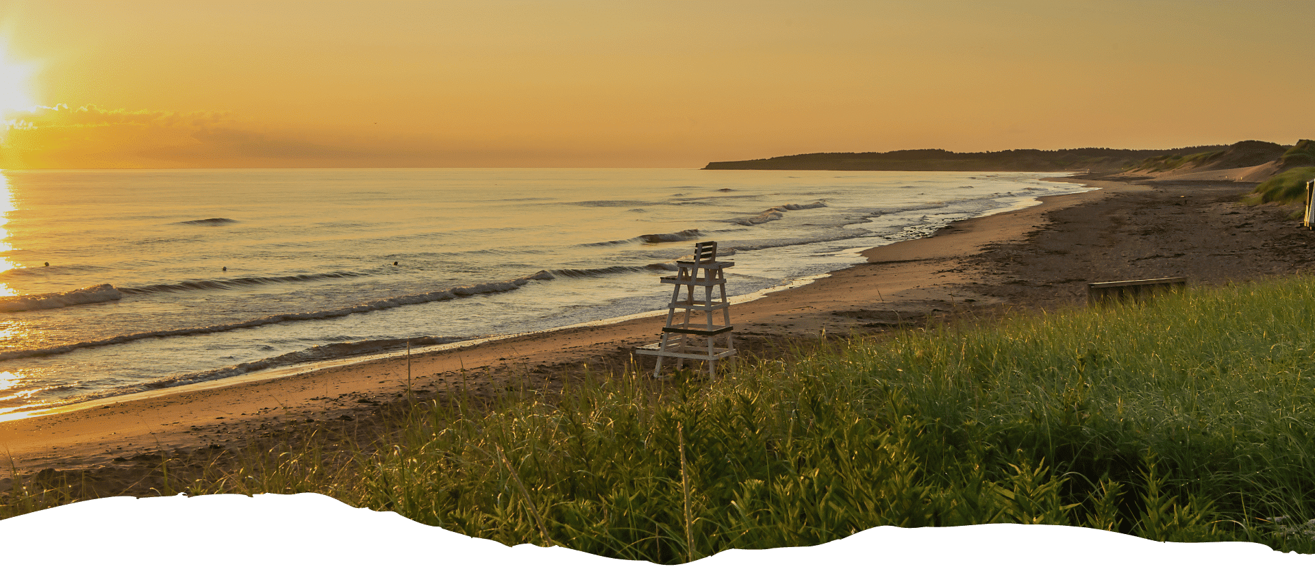 Strandlandschaft mit einem Rettungsschwimmerstuhl und sanften Wellen bei Sonnenuntergang.