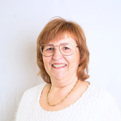 Porträt einer Frau mit braunen Haaren und Brille, die in die Kamera lächelt.