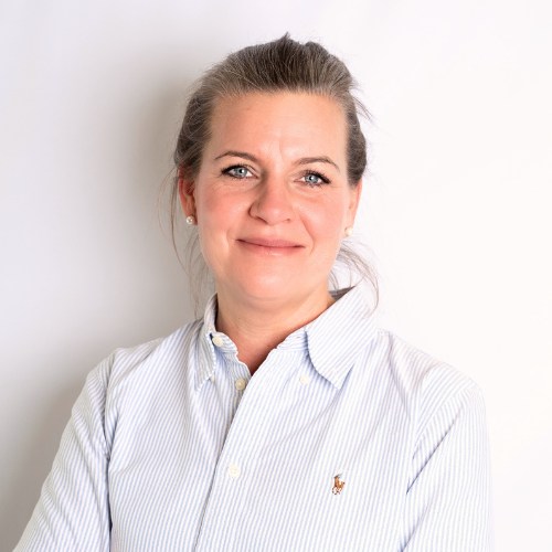 Frau mit blonden Haaren und blauer Bluse, die in die Kamera lächelt.