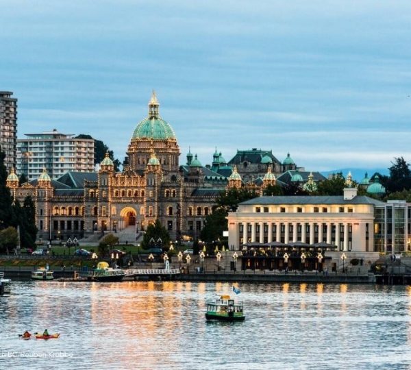 Das Parlamentsgebäude in Victoria, Kanada, beleuchtet bei Dämmerung mit Wasser im Vordergrund.