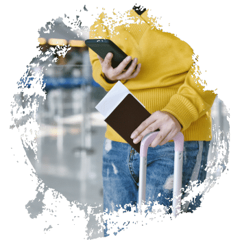 Person in gelbem Pullover hält ein Smartphone und ein Ticket in der Hand, während sie einen Koffer zieht.