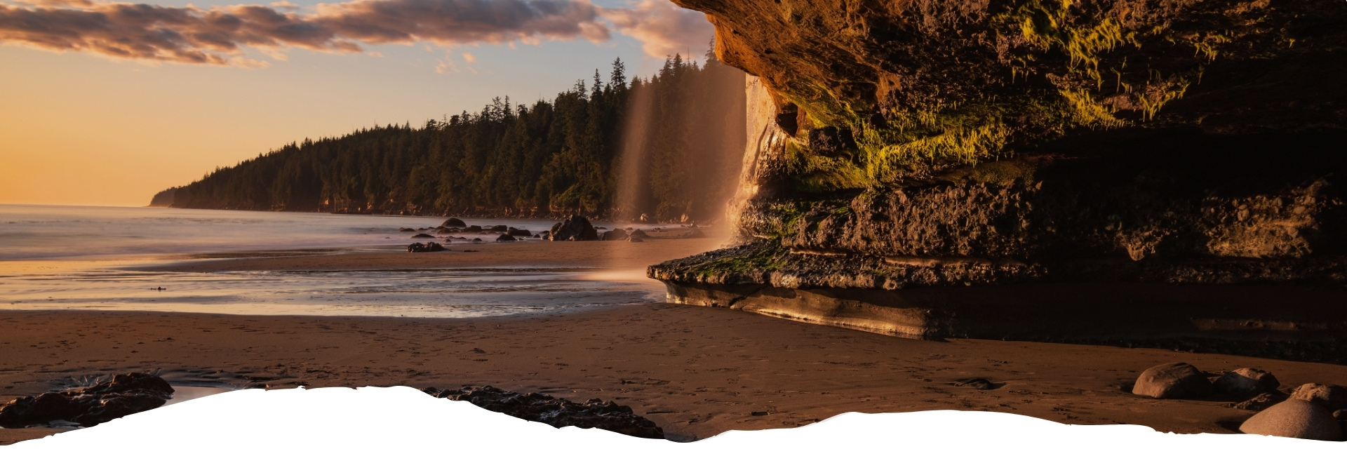 Küstenlandschaft von Vancouver Island mit Felsen und Wasserfall bei Sonnenuntergang.