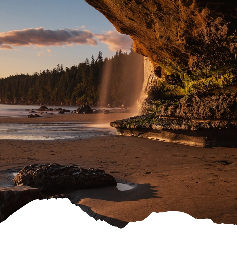 Felsen am Strand mit Wasserfall, der ins Meer fließt, bei Sonnenuntergang.