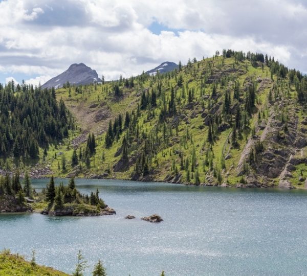 Berglandschaft mit einem klaren See und bewaldeten Hügeln im Hintergrund.