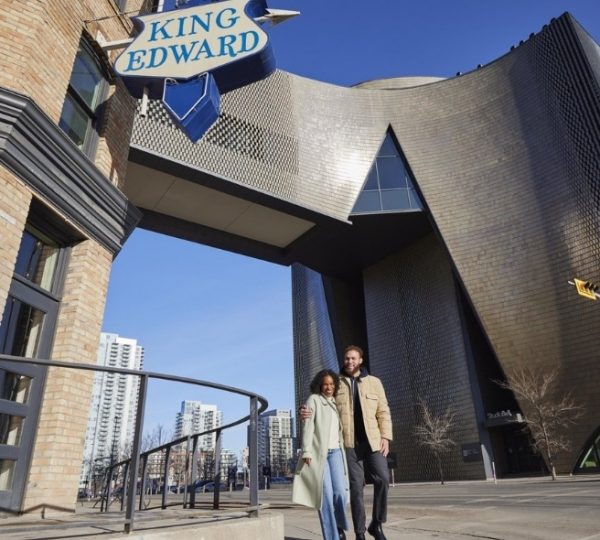 Ein Paar steht vor dem King Edward Gebäude in Calgary, mit einem Schild im Hintergrund.