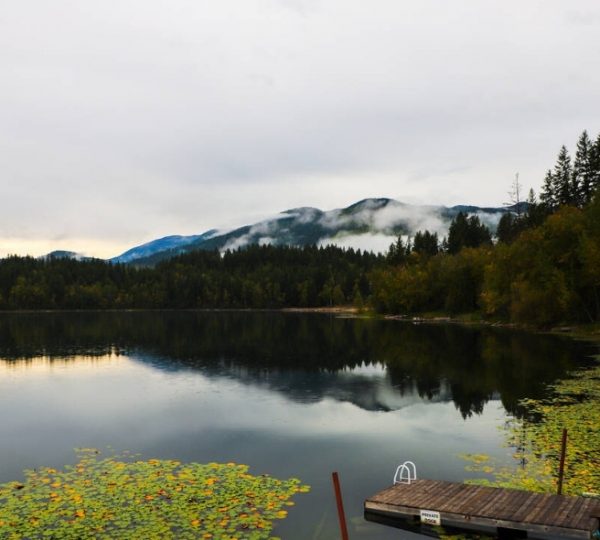 Ruhiges Gewässer mit reflektierenden Bergen und einem Holzsteg im Vordergrund.