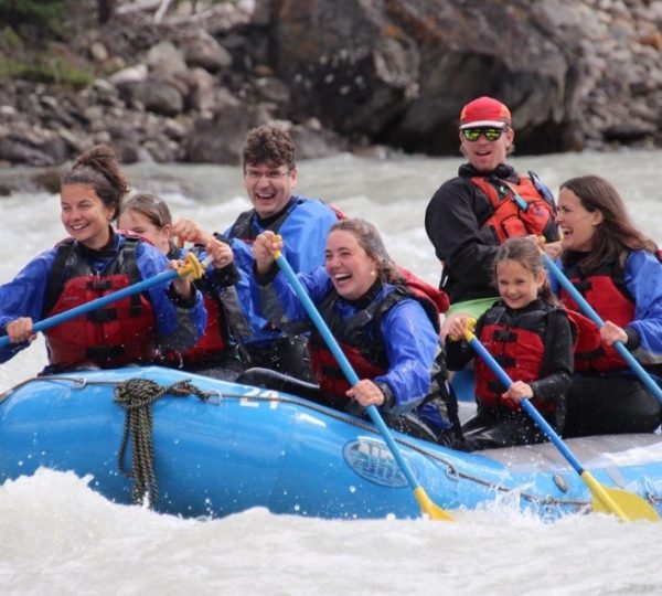Eine Gruppe von sieben Personen im Wildwasser-Rafting auf einem blauen Boot auf einem Fluss.