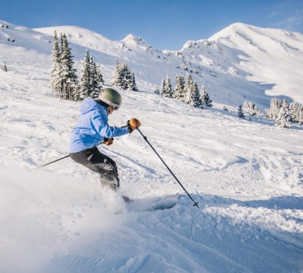 Ein Skifahrer in blauer Jacke und Helm fährt eine verschneite Piste hinunter.