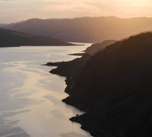 Blick auf den Kamloops-See mit sanften Hügeln und Sonnenuntergang im Hintergrund.