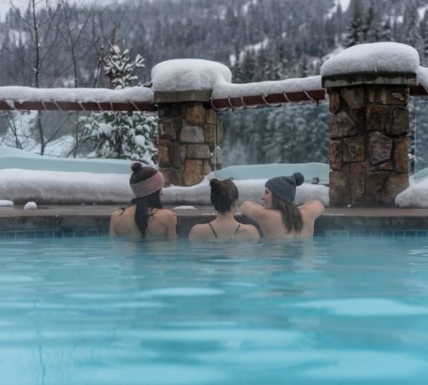 Drei Frauen in einem Außenwhirlpool, umgeben von Schnee und Bäumen im Winter.