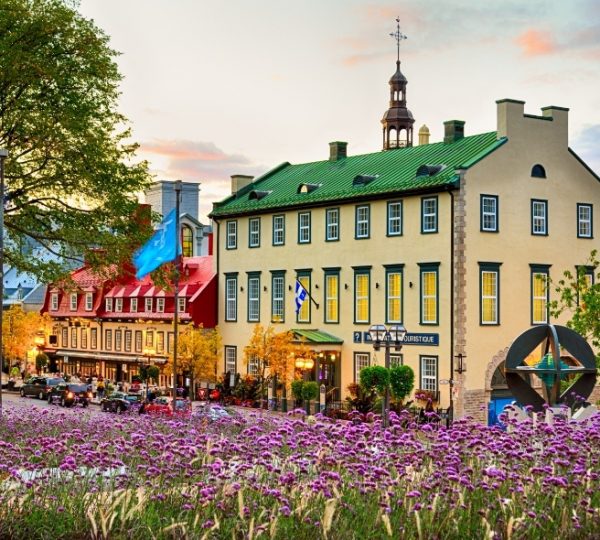 Historisches Gebäude in Quebec City mit grünem Dach und bunten Blumen im Vordergrund.