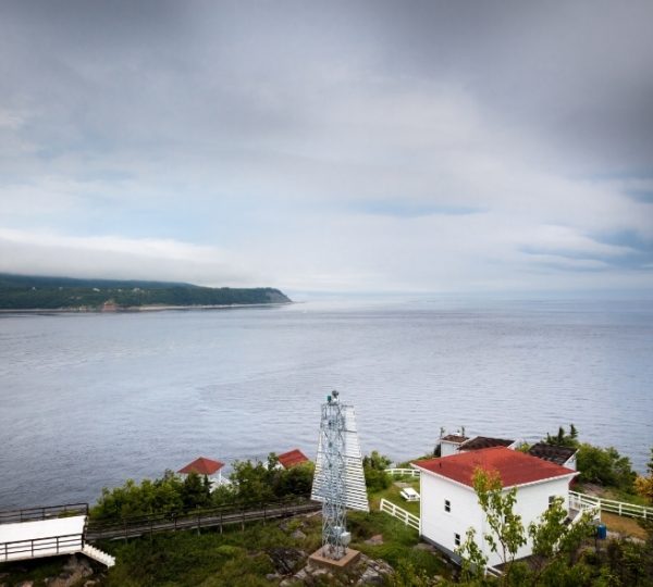 Leuchtturm mit rotem Dach und angrenzendem Gebäude an der Küste von Tadoussac.