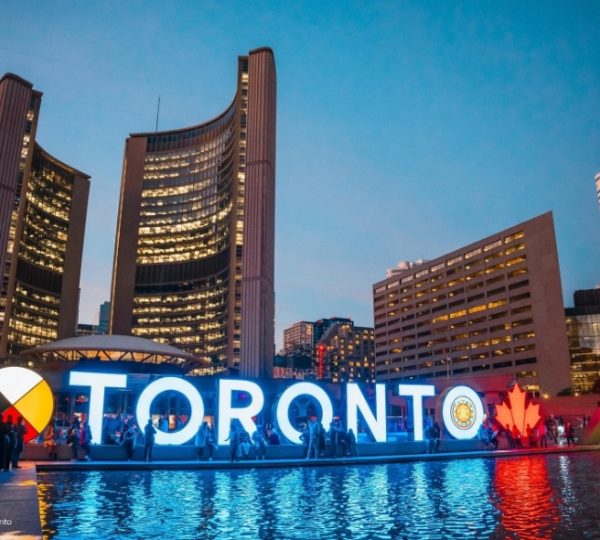 Beleuchtetes Toronto-Schild mit Stadtgebäuden im Hintergrund bei Dämmerung am Nathan Phillips Square.