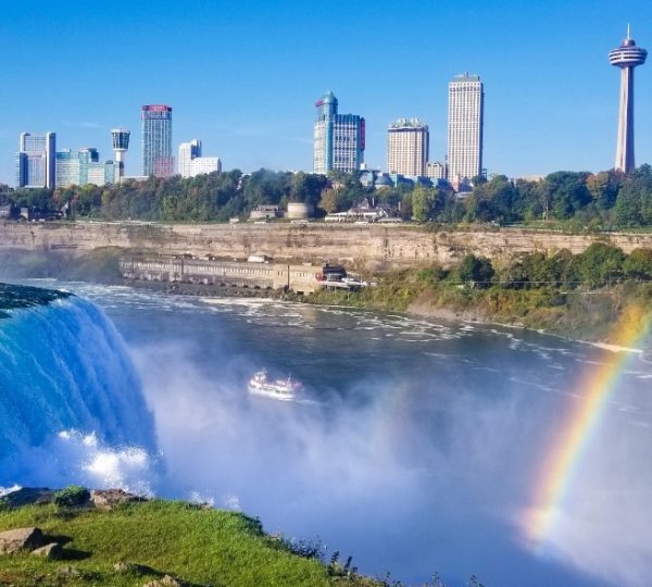 Niagarafälle mit einem Regenbogen und einer Stadtansicht im Hintergrund, inklusive Wolkenkratzern.
