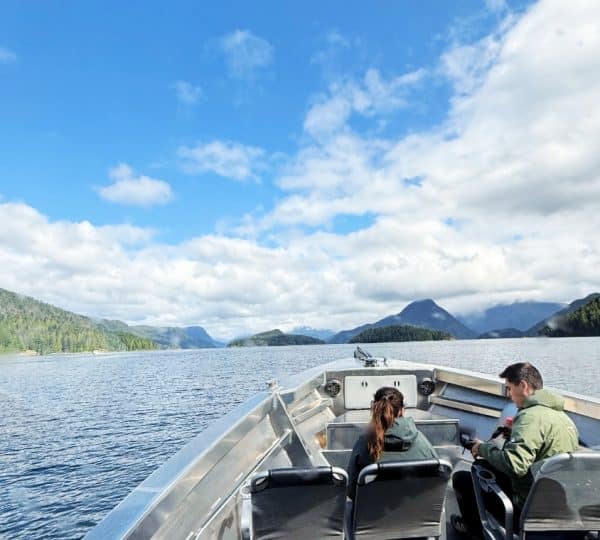 Personen sitzen auf einem Boot während einer Fahrt durch die Gewässer von Westkanada mit Bergen im Hintergrund.