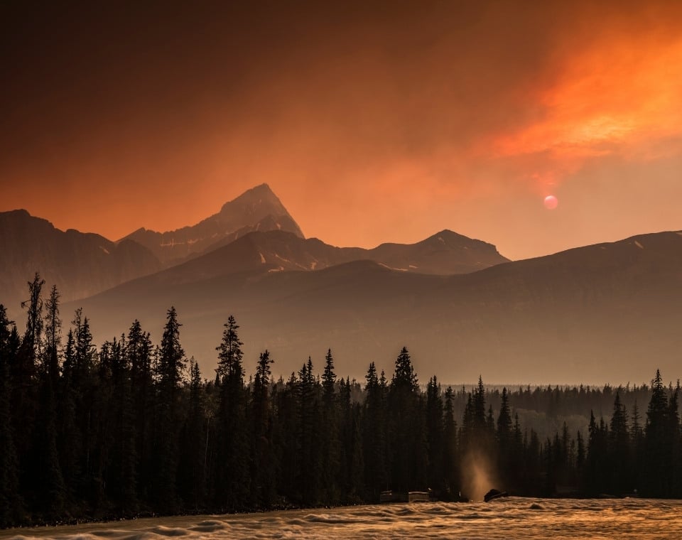 Berglandschaft mit rauchigem Himmel und untergehender Sonne in Kanada.