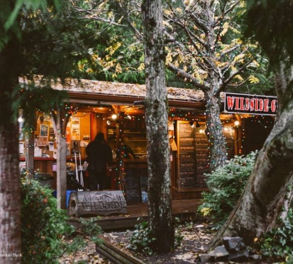Holzhütte mit warmem Licht und Schildern, umgeben von Bäumen in einer natürlichen Umgebung.