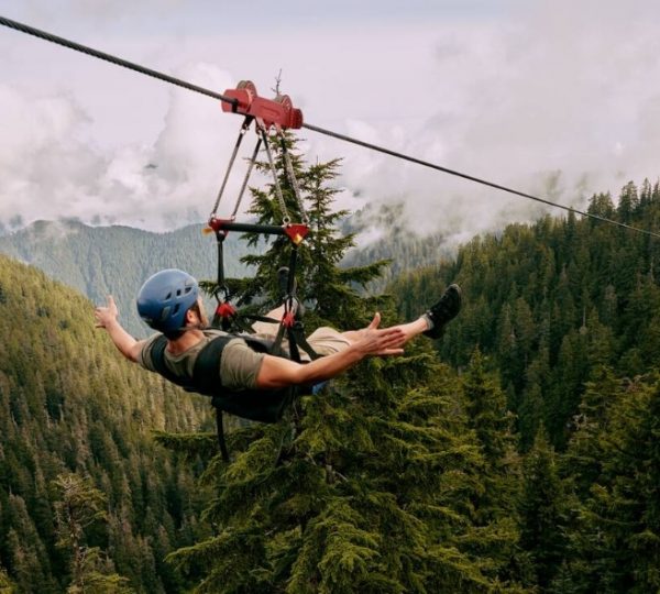 Mann in einem blauen Helm, der an einem Seil durch einen Wald in den Bergen zippt. Kanada-Rundreise