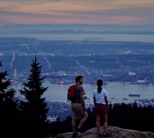 Ein Paar steht auf einem Aussichtspunkt und blickt auf die Stadt Vancouver bei Sonnenuntergang. Kanada-Rundreise