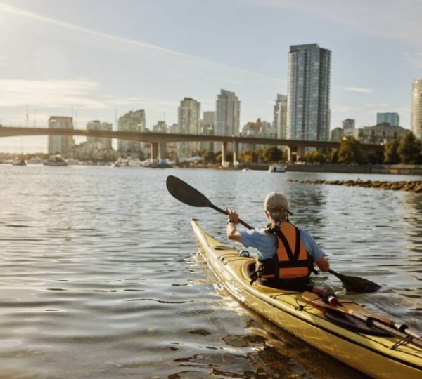 Ein Kajakfahrer paddelt auf dem Wasser mit einer Stadtansicht im Hintergrund in Vancouver. Kanada-Rundreise