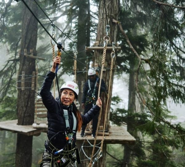 Eine Person in Sicherheitsausrüstung beim Ziplining zwischen Bäumen in einem Waldgebiet. Kanada-Rundreise