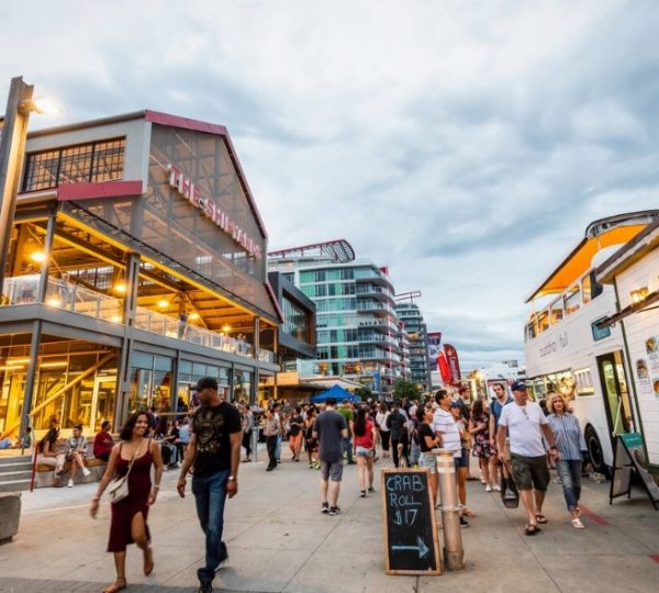 Belebte Straße mit Geschäften, Menschen und Ständen in einer urbanen Umgebung bei bewölktem Himmel. Kanada-Rundreise