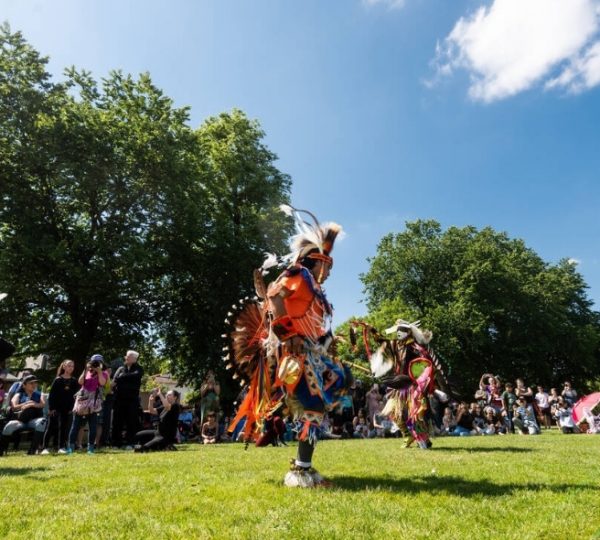 Tänzer in bunter traditioneller Kleidung führen einen Tanz vor einer Menschenmenge im Freien auf. Kanada-Rundreise