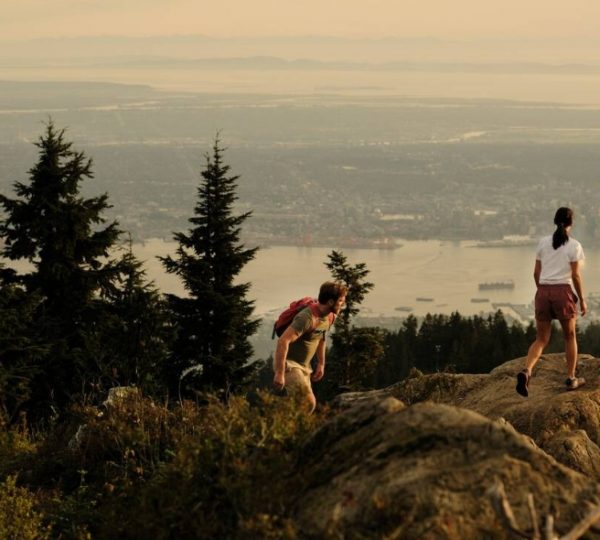 Zwei Wanderer auf einem Felsen mit Blick auf die Stadt Vancouver und das Wasser im Hintergrund. Kanada-Rundreise
