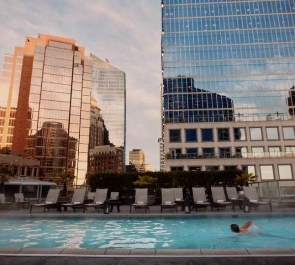 Schwimmbad mit einer Person, umgeben von modernen Gebäuden und reflektierenden Fenstern. Kanada-Rundreise