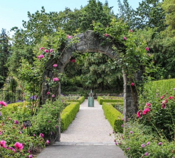 Ein Garten mit einem Steinbogen, umgeben von bunten Blumen und grünen Hecken. Kanada-Rundreise