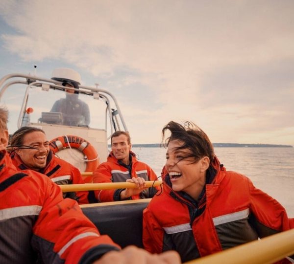 Vier Personen in roten Schwimmwesten sitzen in einem Zodiac-Boot auf dem Wasser und lachen. Kanada-Rundreise
