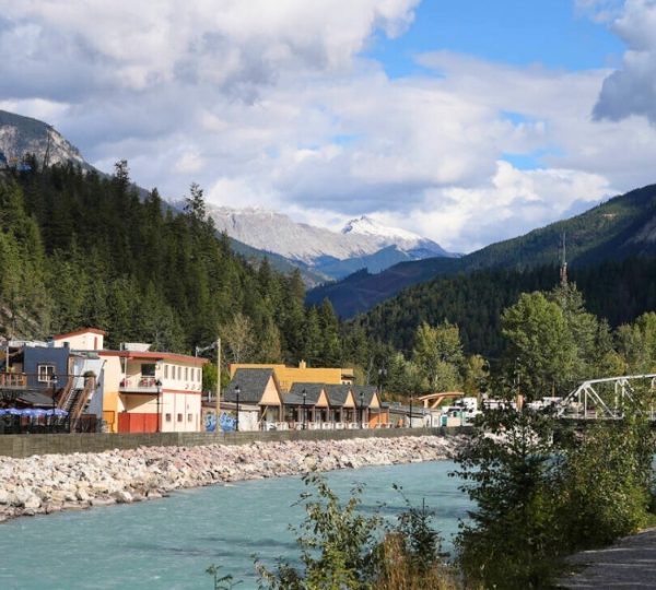 Fluss mit klaren, blauen Wasser und Gebäuden am Ufer, umgeben von Bergen und Bäumen.