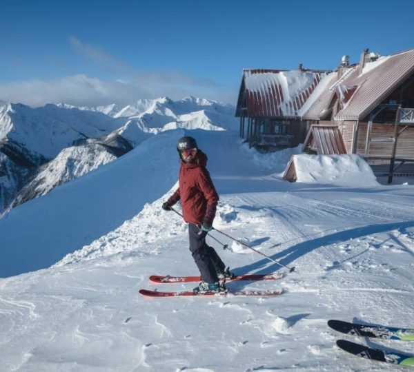 Skifahrer in roter Jacke auf einem verschneiten Hang mit Bergen im Hintergrund. Kanada-Rundreise