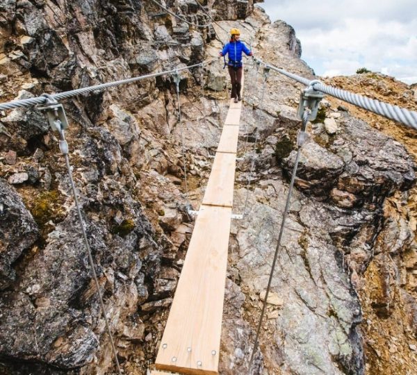 Eine Person in blauer Kleidung geht über eine Hängebrücke aus Holz zwischen Felsen in den Rocky Mountains. Kanada-Rundreise