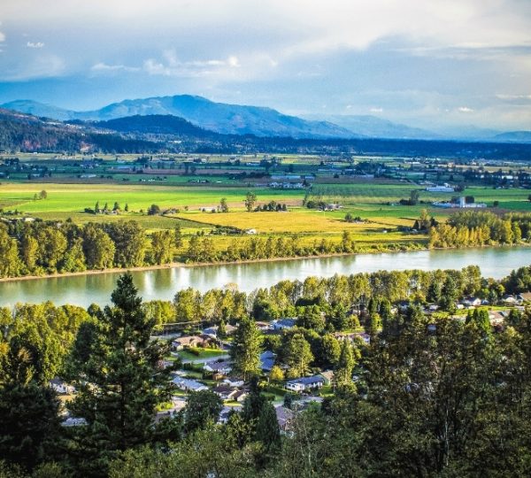 Landschaftsaufnahme mit einem Fluss, umgeben von Bäumen und Bergen im Hintergrund in Westkanada. Kanada-Rundreise