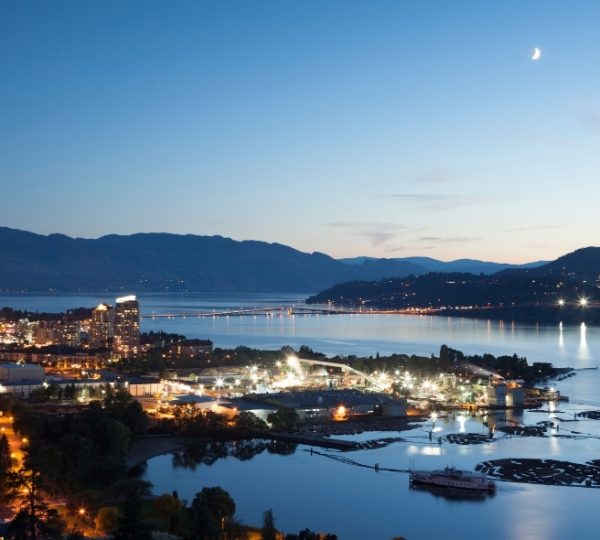 Nachtaufnahme von Kelowna mit beleuchteten Gebäuden und dem Okanagansee im Hintergrund. Kanada-Rundreise