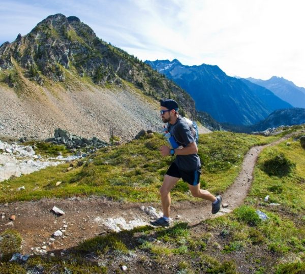Ein Läufer, der einen Bergpfad in den kanadischen Rocky Mountains entlangläuft, umgeben von Bergen und Natur. Kanada-Rundreise