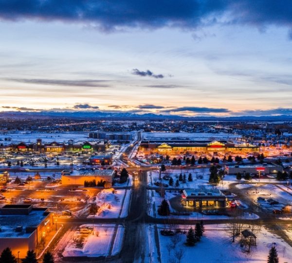 Luftaufnahme von Bozeman, Montana, mit beleuchteten Geschäften und schneebedeckten Straßen bei Sonnenuntergang. Kanada-Rundreise