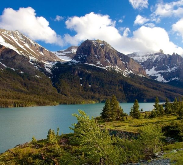 Berglandschaft mit schneebedeckten Gipfeln und einem ruhigen See im Vordergrund. Kanada-Rundreise