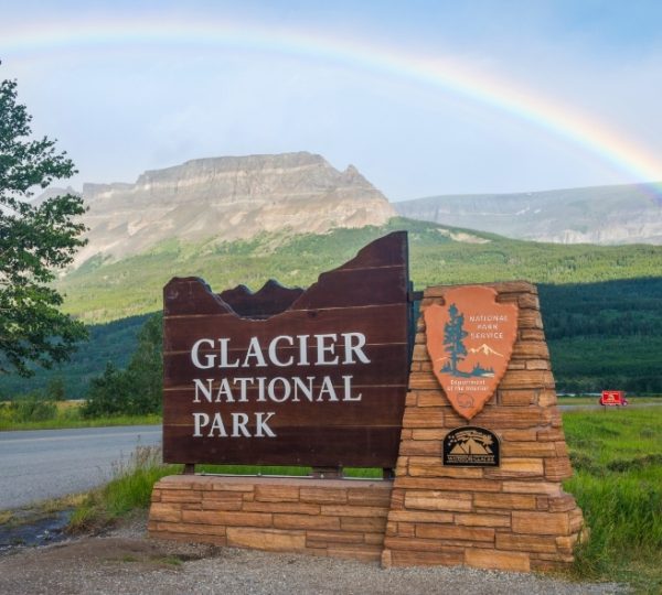 Holzschild mit der Aufschrift 'Glacier National Park' und einem Regenbogen im Hintergrund. Kanada-Rundreise
