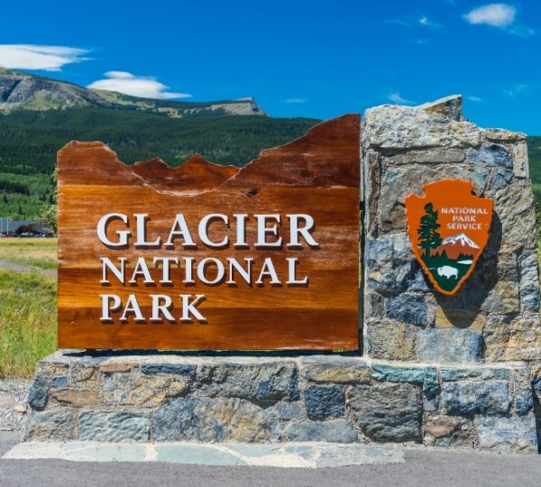 Holz- und Steinschild mit der Aufschrift 'Glacier National Park' und dem Logo des National Park Service. Kanada-Rundreise