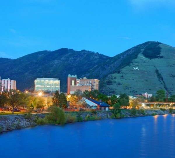 Blick auf die Stadt Missoula mit Bergen und einem Fluss bei Dämmerung. Kanada-Rundreise