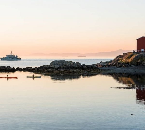 Leuchtturm auf Vancouver Island mit zwei Kajakfahrern im Wasser und einem Schiff im Hintergrund. Kanada-Rundreise