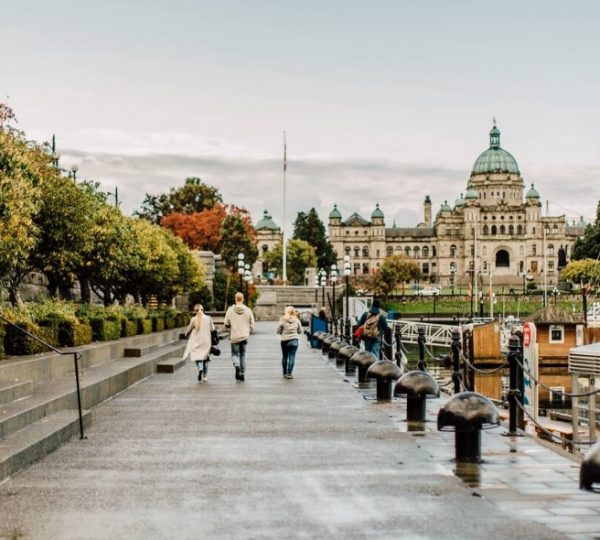 Personen gehen entlang des Inner Harbour in Victoria, mit den Parlamentsgebäuden im Hintergrund. Kanada-Rundreise