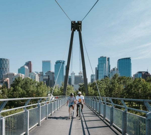 Zwei Personen gehen über eine Brücke in Calgary mit der Skyline im Hintergrund. Kanada-Rundreise