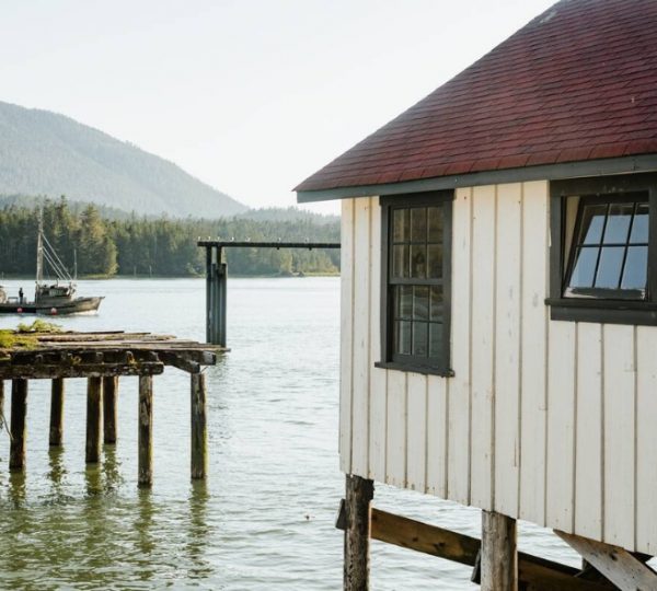 Ein Holzhaus mit rotem Dach steht am Wasser, während ein Boot in der Nähe fährt. Kanada-Rundreise