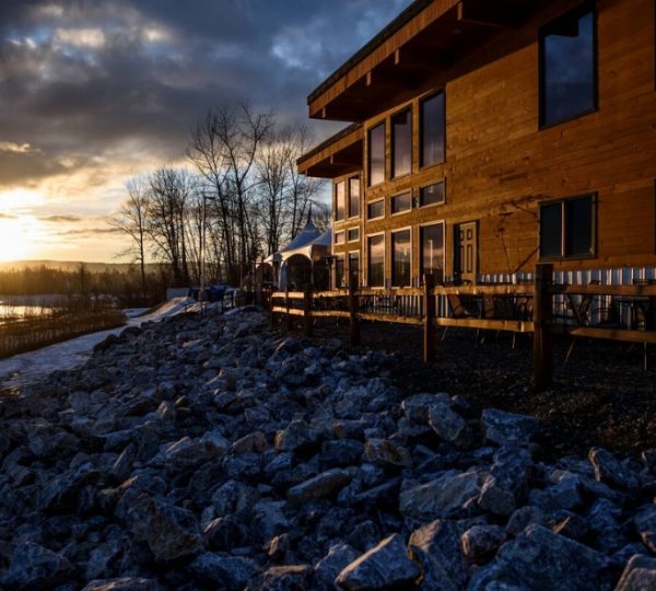 Holzgebäude mit großen Fenstern und Terrasse am Wasser bei Sonnenuntergang. Kanada-Rundreise