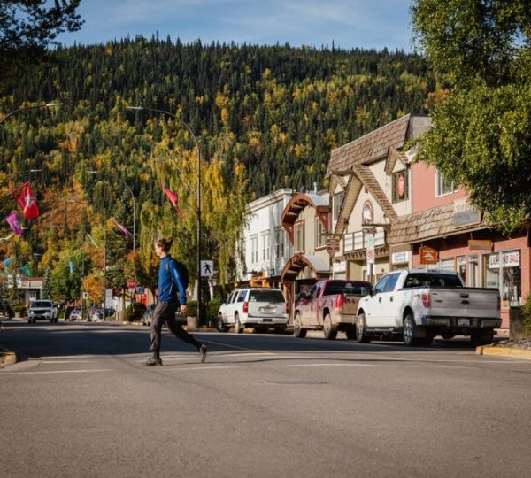 Person überquert eine Straße in Smithers, umgeben von Geschäften und Fahrzeugen. Kanada-Rundreise