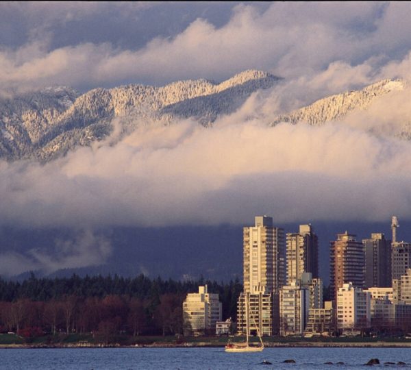 Hochhäuser in Vancouver mit schneebedeckten Bergen im Hintergrund und Wolken am Himmel. Kanada-Rundreise