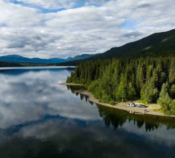 Ruhige Wasseroberfläche des Dease Lake mit umliegenden Wäldern und Bergen in Westkanada. Kanada-Rundreise